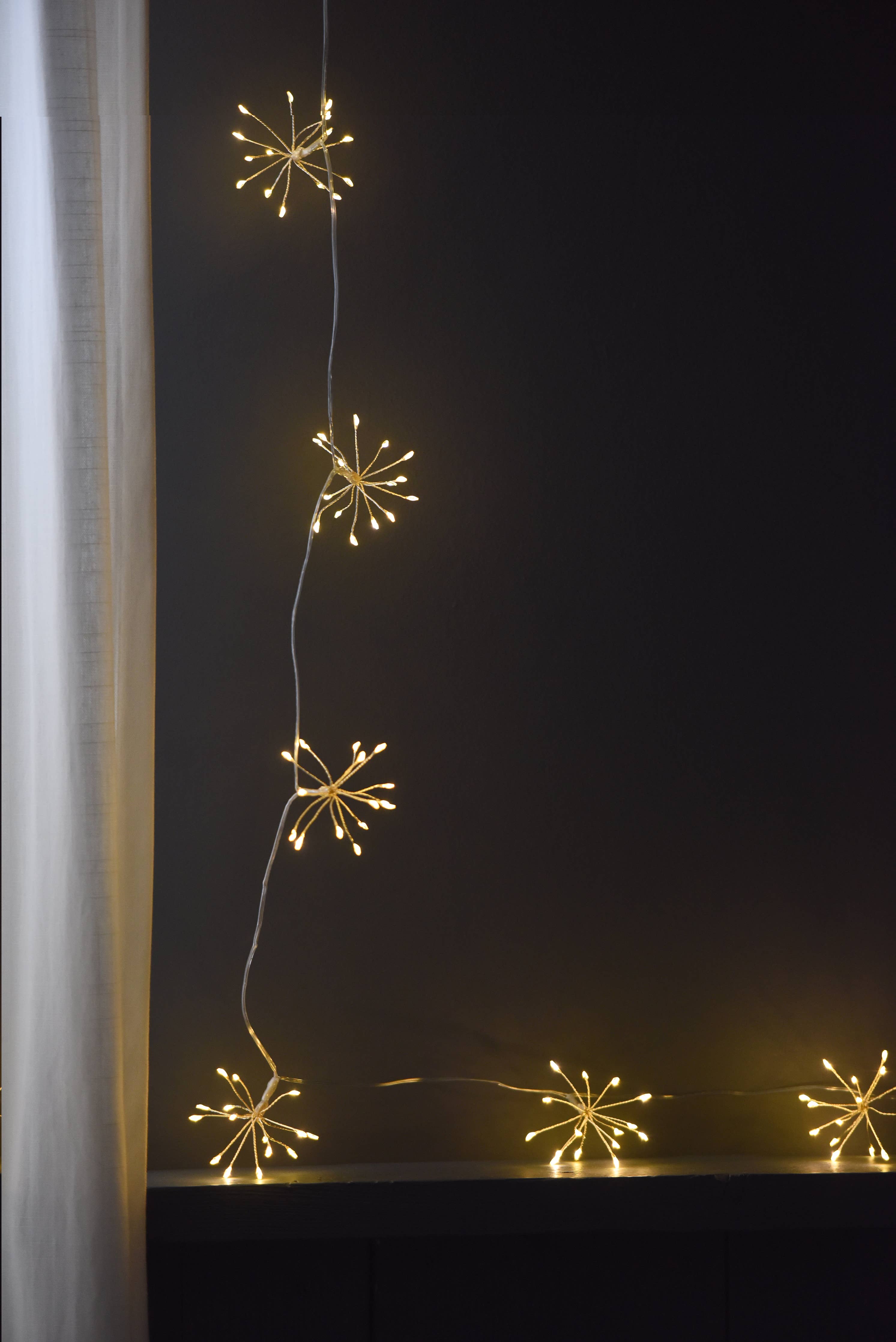 Golden starburst LED string lights on black battery chain, warm glow