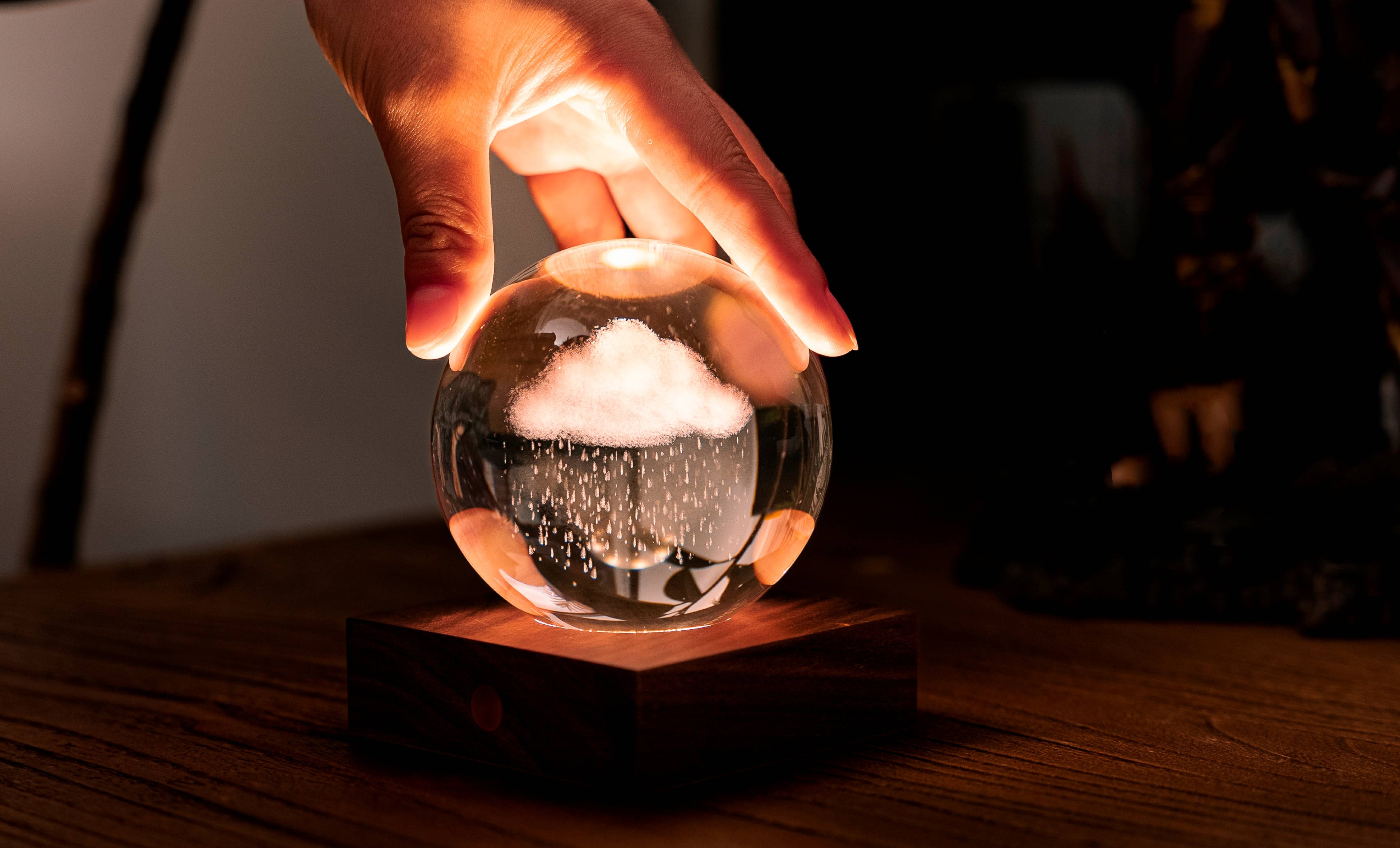 Hand holding glowing Amber Crystal Light globe with mini cloud and rain