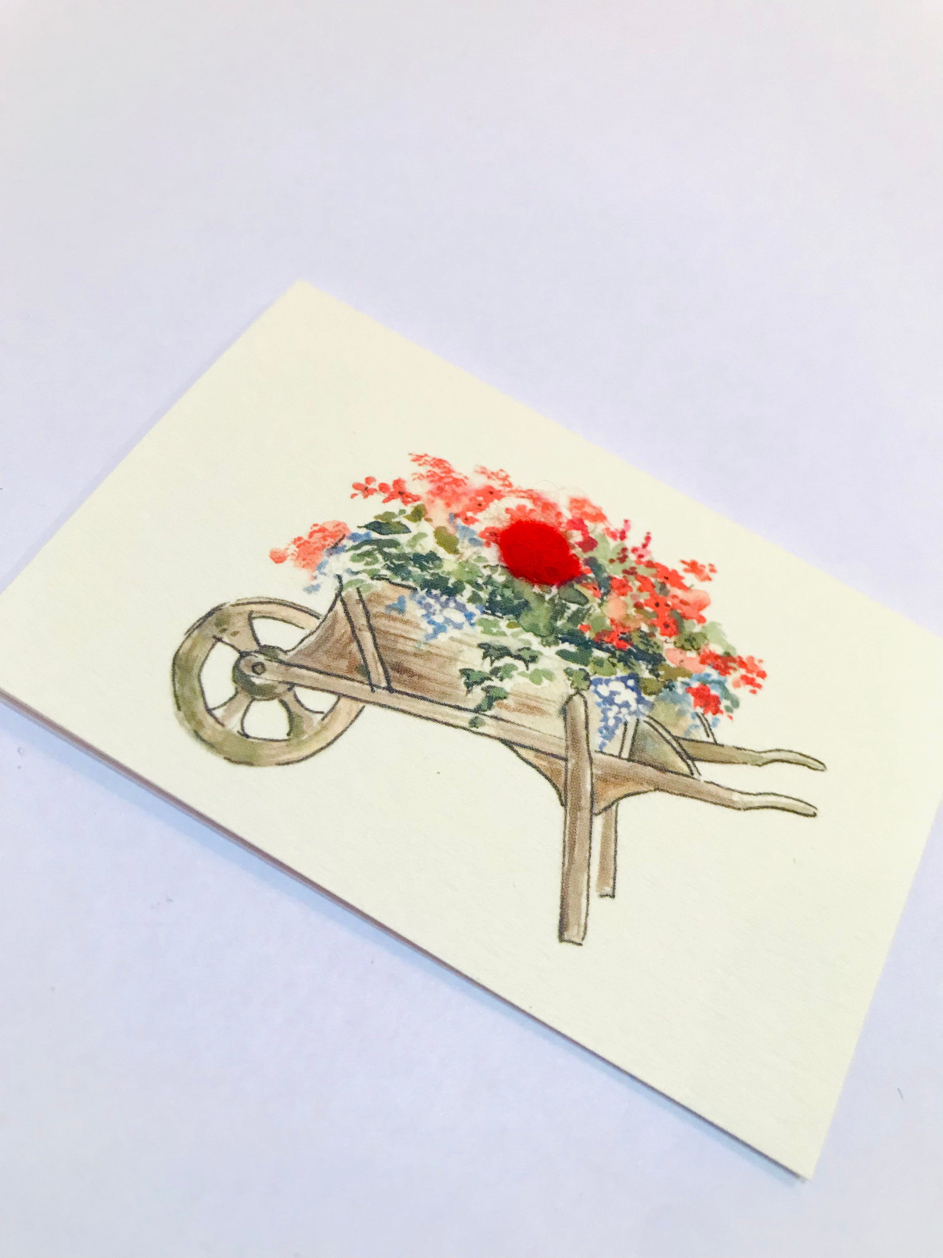 Watercolor mini wheelbarrow overflowing with red and blue flowers on card