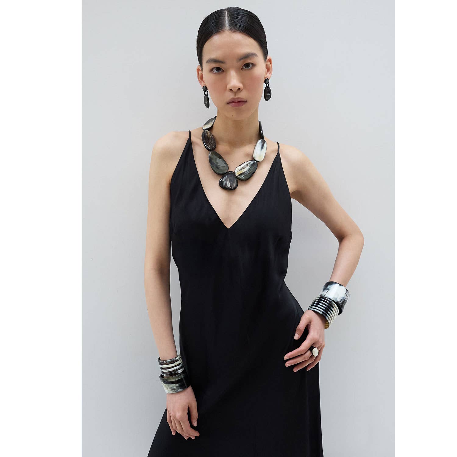 Black satin slip dress with deep V-neck and oval horn cocktail ring