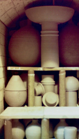 Beige ceramic pedestal sink with rounded basin and fluted base on arched shelf.