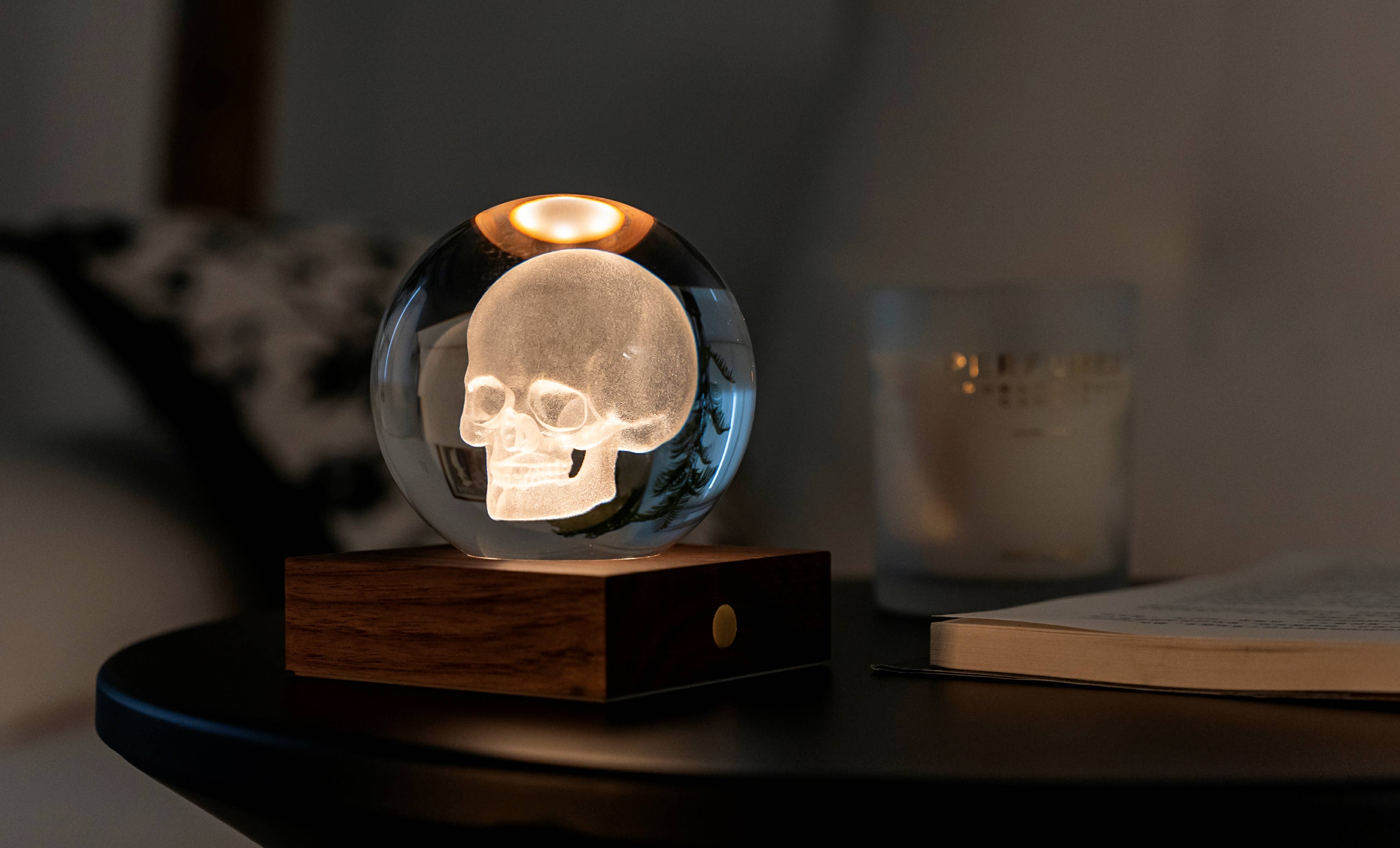 Translucent glass skull orb lamp with warm amber light on dark wood base