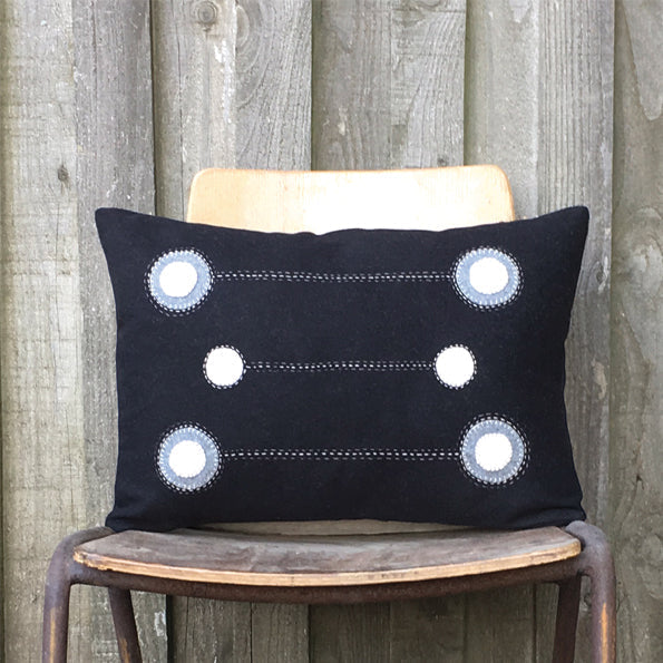 Black wool cushion with white and gray circular appliques connected by stitched lines