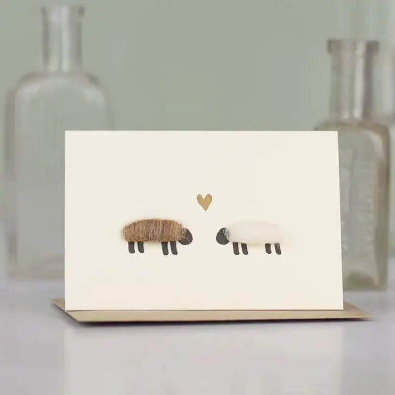 Cream-colored greeting card with two sheep and a heart design, featuring brown wool texture on one sheep.