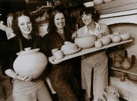 Three women in pottery studio holding handmade ceramic pots and bowls