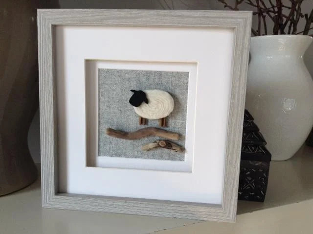 One Sheep: white felt sheep with black face and brown legs on driftwood in gray frame