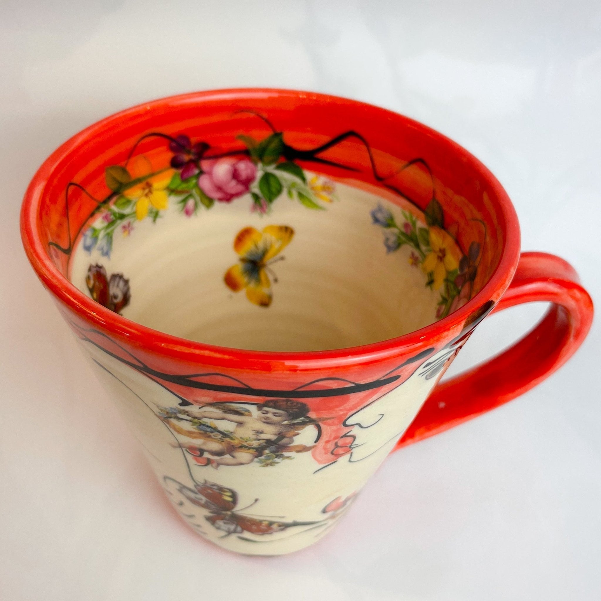 Vibrant red ceramic mug with floral and butterfly designs on cream background