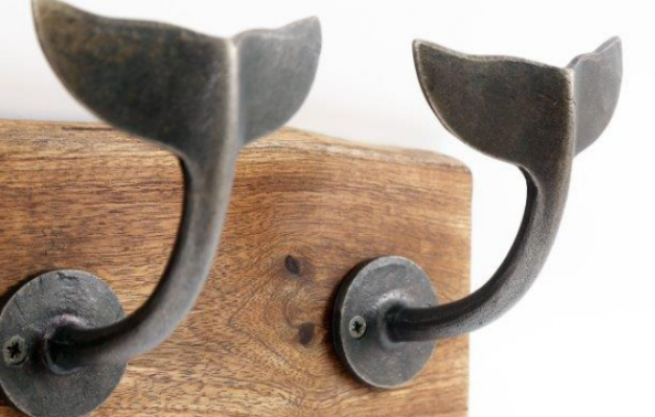 Row of four dark gray metal whale tail hooks on wooden board